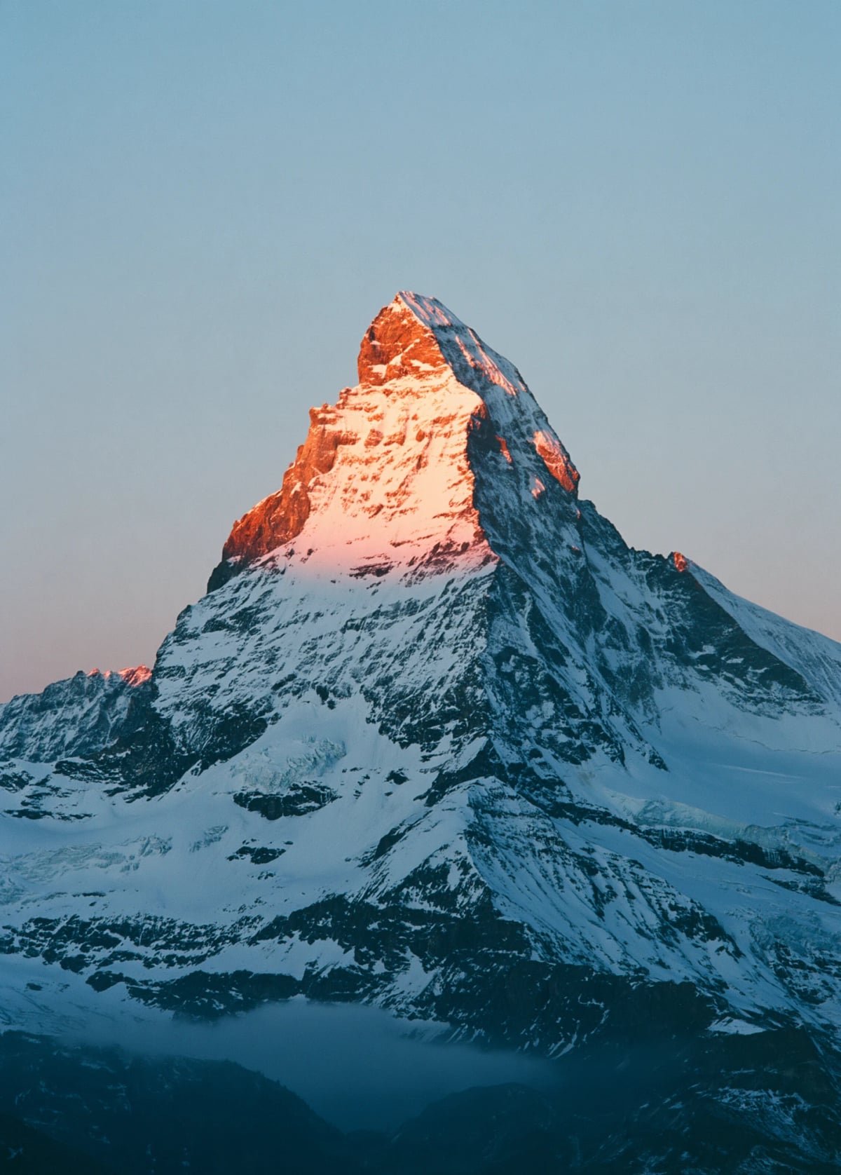 A snow-covered peak lit rose by the first sunrise, the slopes below still in blue shadow